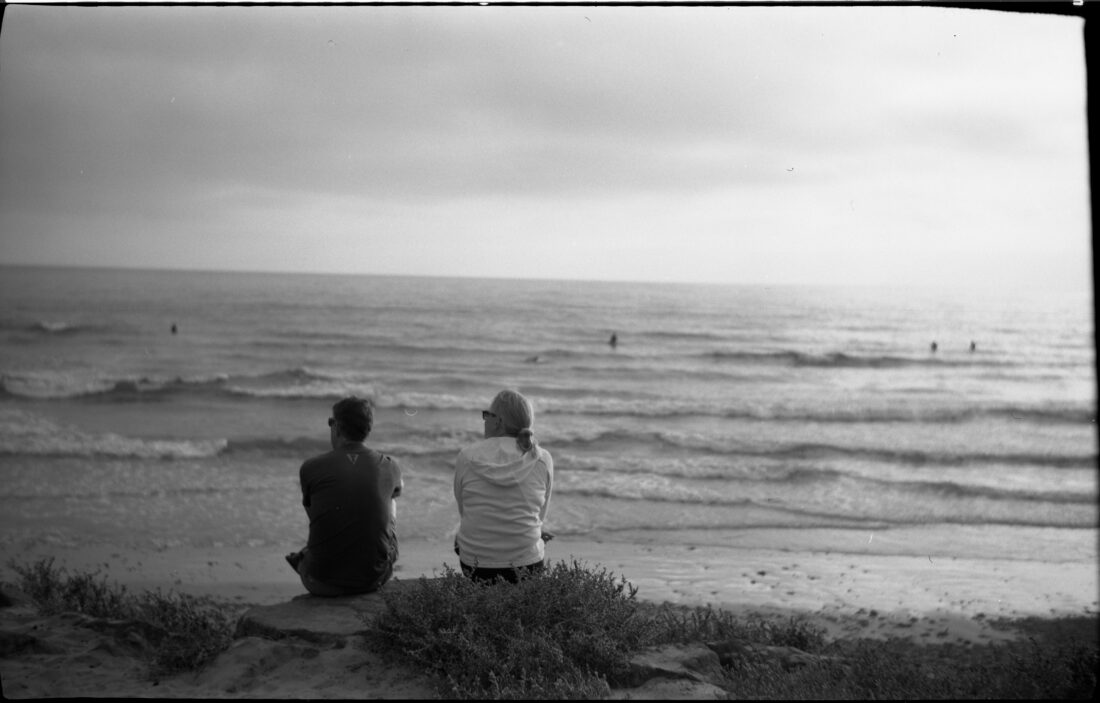 two people sitting on a rock overlooking the ocean